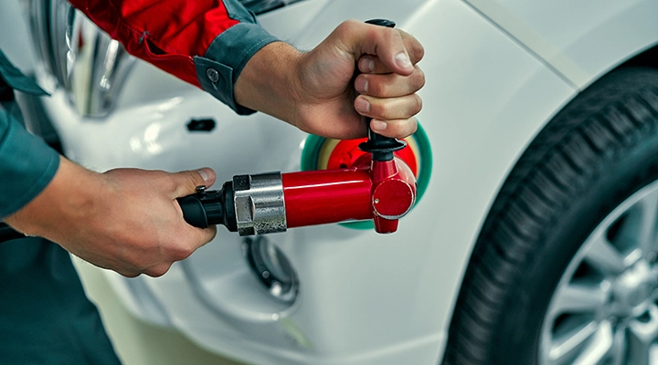 Technician using paintless dent repair pulling tool to remove dent from car panel without damaging paint
