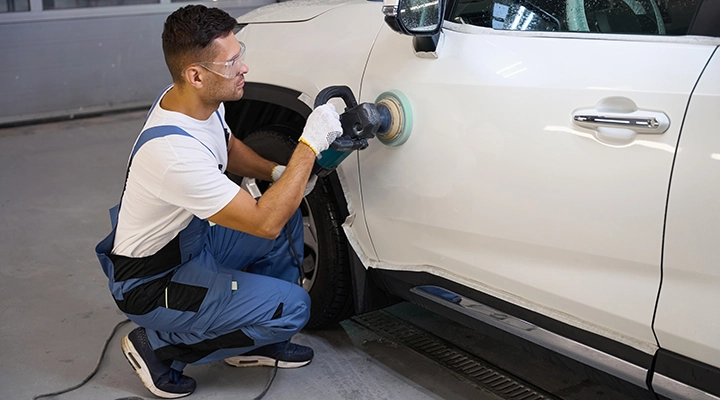 Auto technician polishing a white SUV door with a power buffer to remove scratches and restore the paint finish.