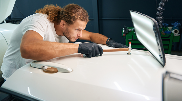 Paintless dent repair technician using precision tools and LED light to remove dent from car panel without repainting